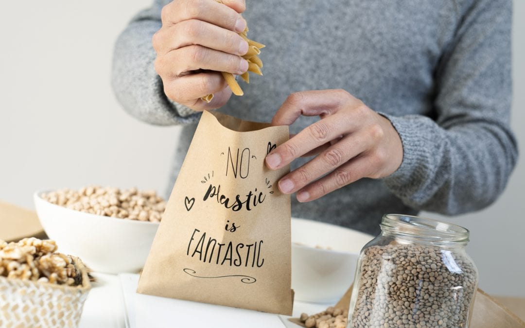 closeup of a man putting some dry macaroni on a brown paper bag, with the text no plastic is fantastic written in it, placed on an electronic scale
